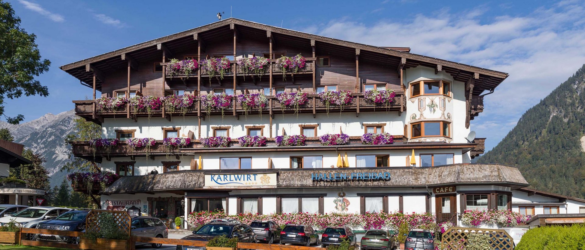 New at the Karlwirt: our website! Hotel building with flowers and cars parked in front in the Alps