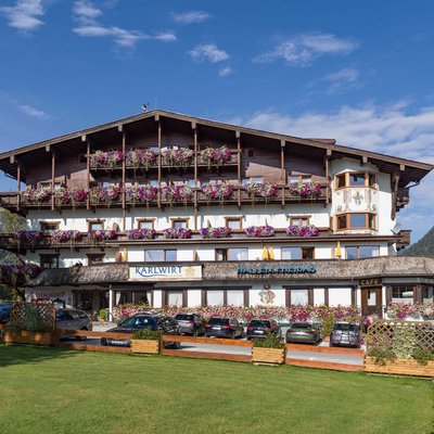 Hotel Karlwirt: a warm welcome! Hotel building with flowers and cars parked in front in the Alps