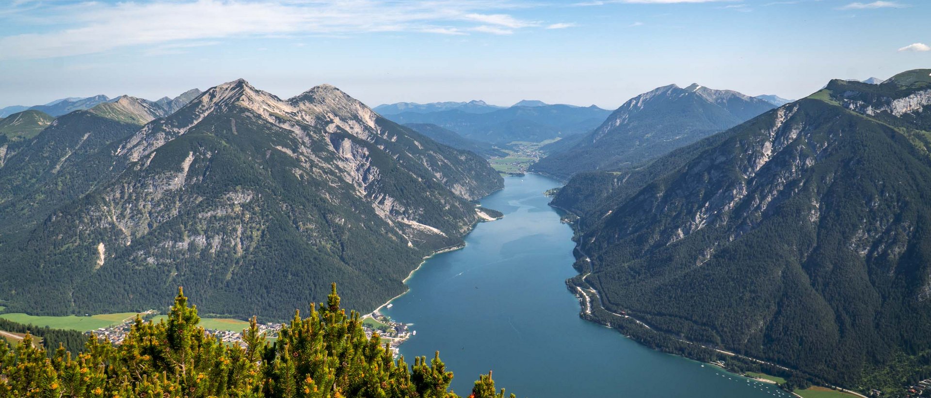 Der AIRROFAN Skyglider Bergsee umgeben von bewaldeten Bergen unter blauem Himmel