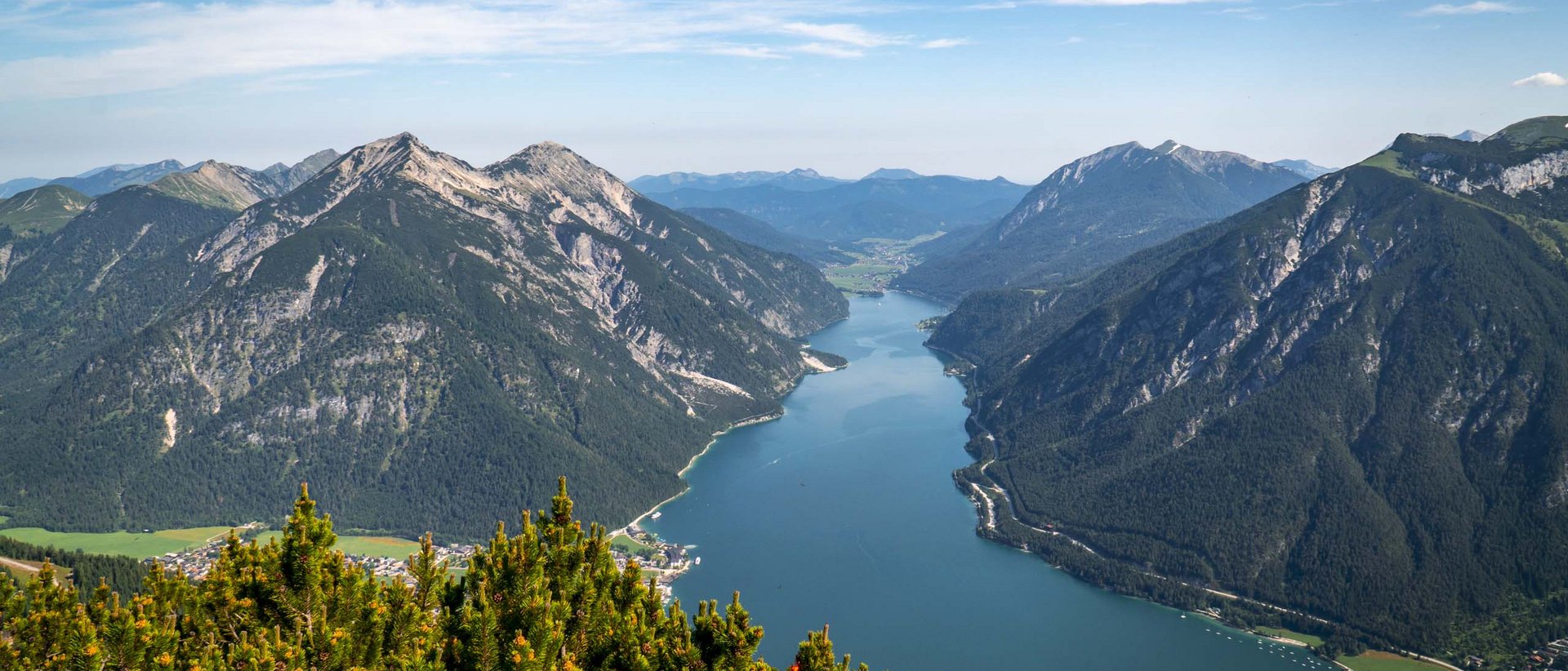 Der AIRROFAN Skyglider Bergsee umgeben von bewaldeten Bergen unter blauem Himmel