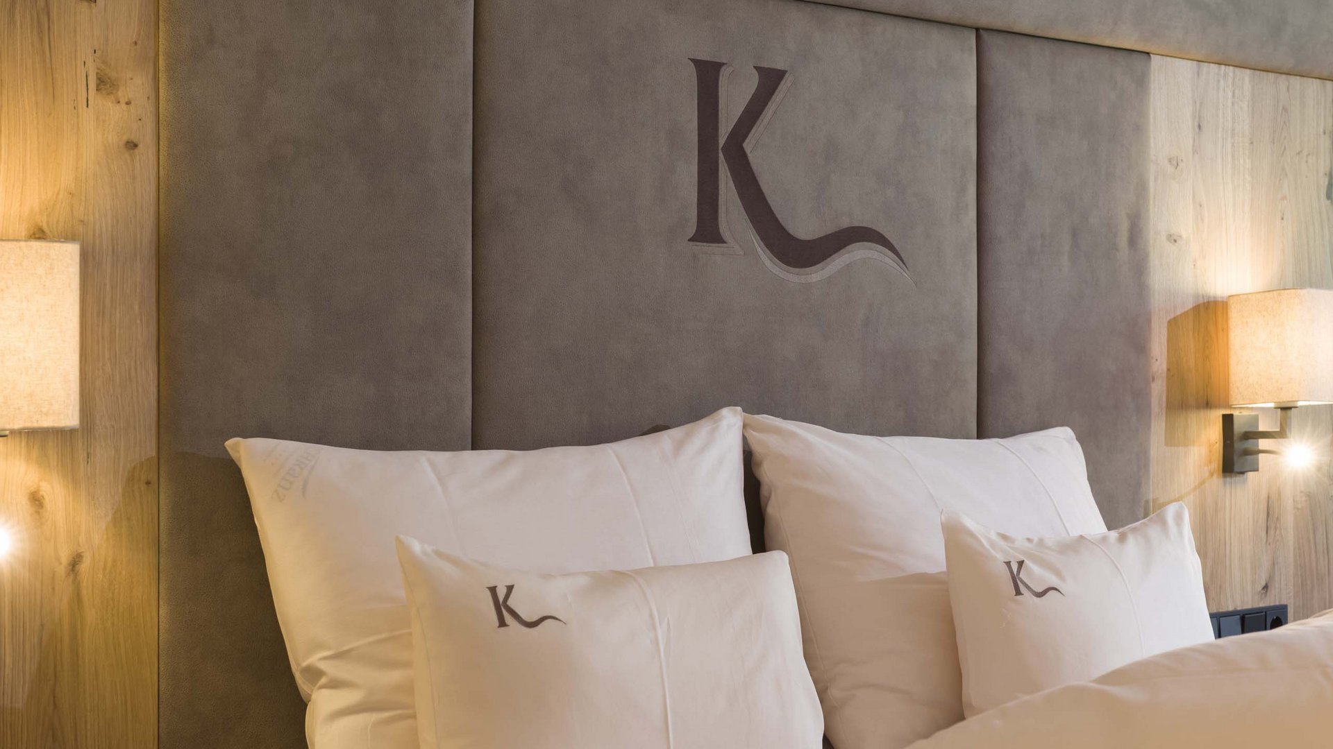 Bett mit weißen Kissen und Kopfteil mit Logo in modern eingerichteter Zimmer