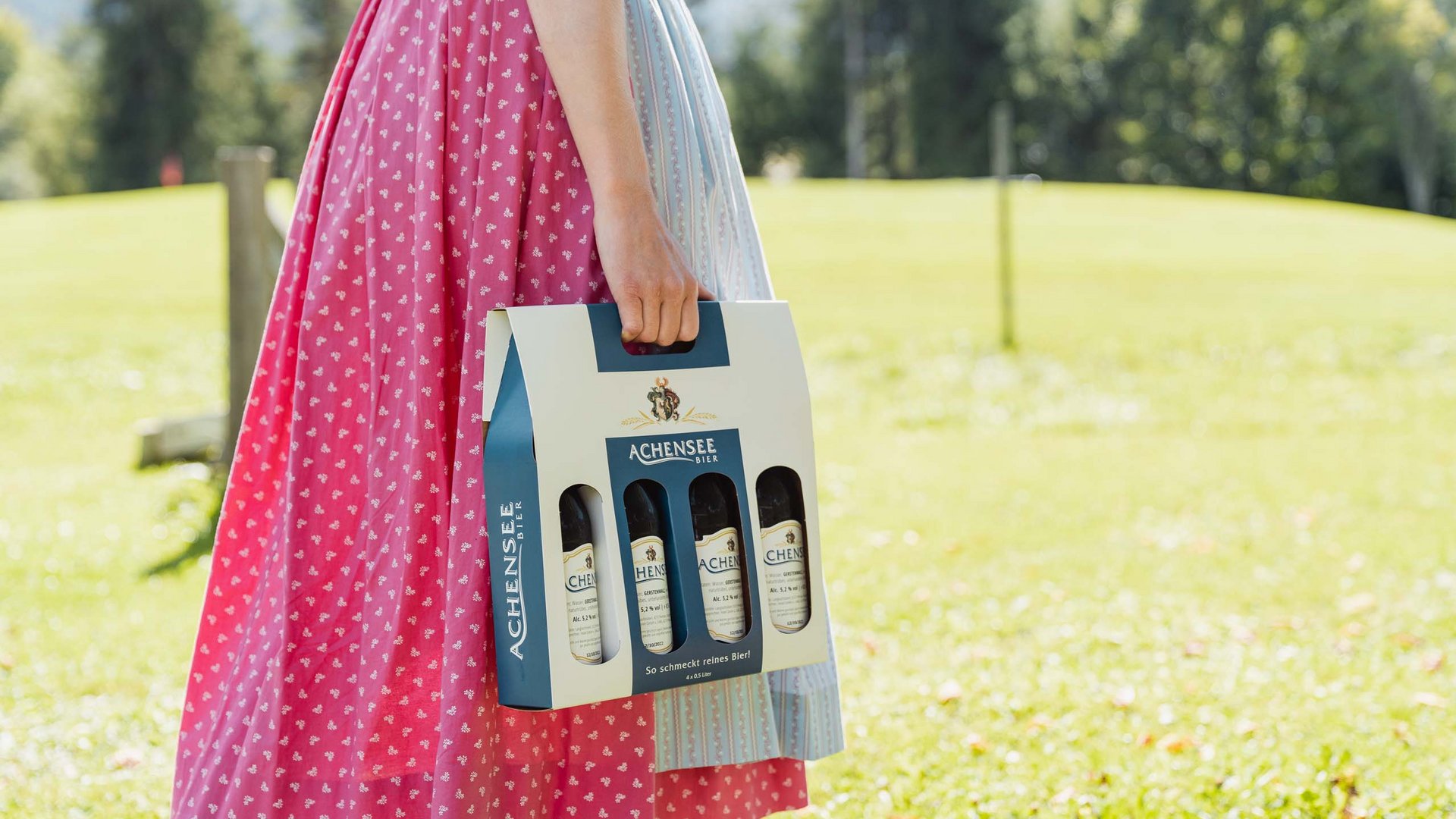 Das Achenseebier des Karlwirt Person in Dirndl trägt 4er-Pack Achensee Bier im Freien