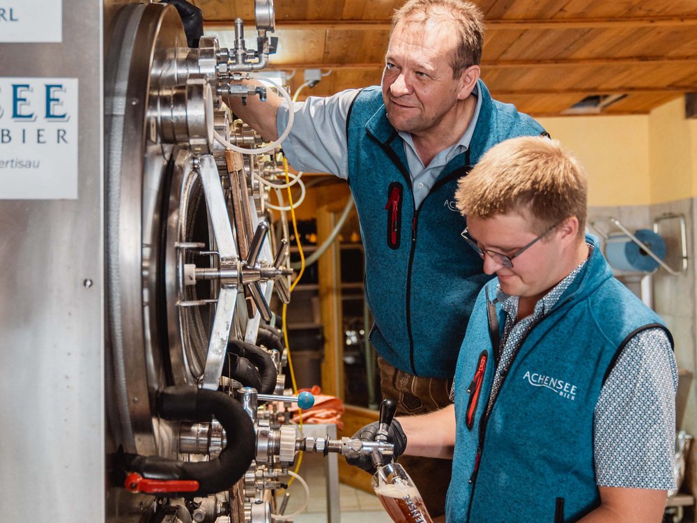 Das Achenseebier des Karlwirt Zwei Männer zapfen Bier aus Metallfässern in einer Brauerei